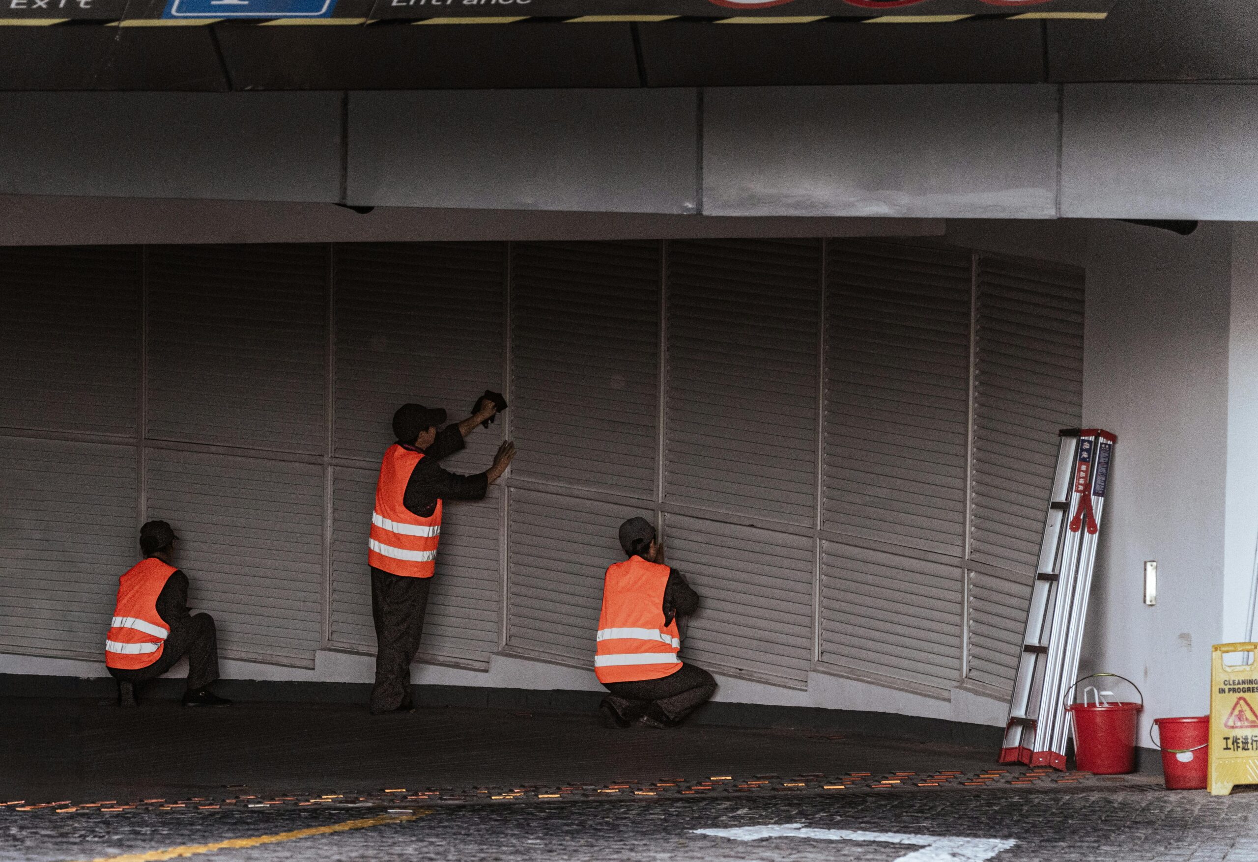 Three workers in safety vests install security shutters at an indoor entrance.